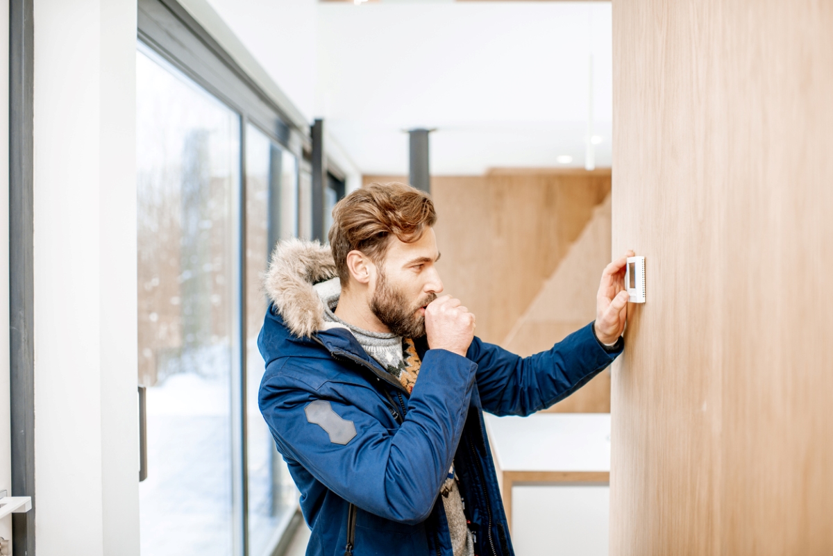 Man wearing jacket adjusting home thermostat.