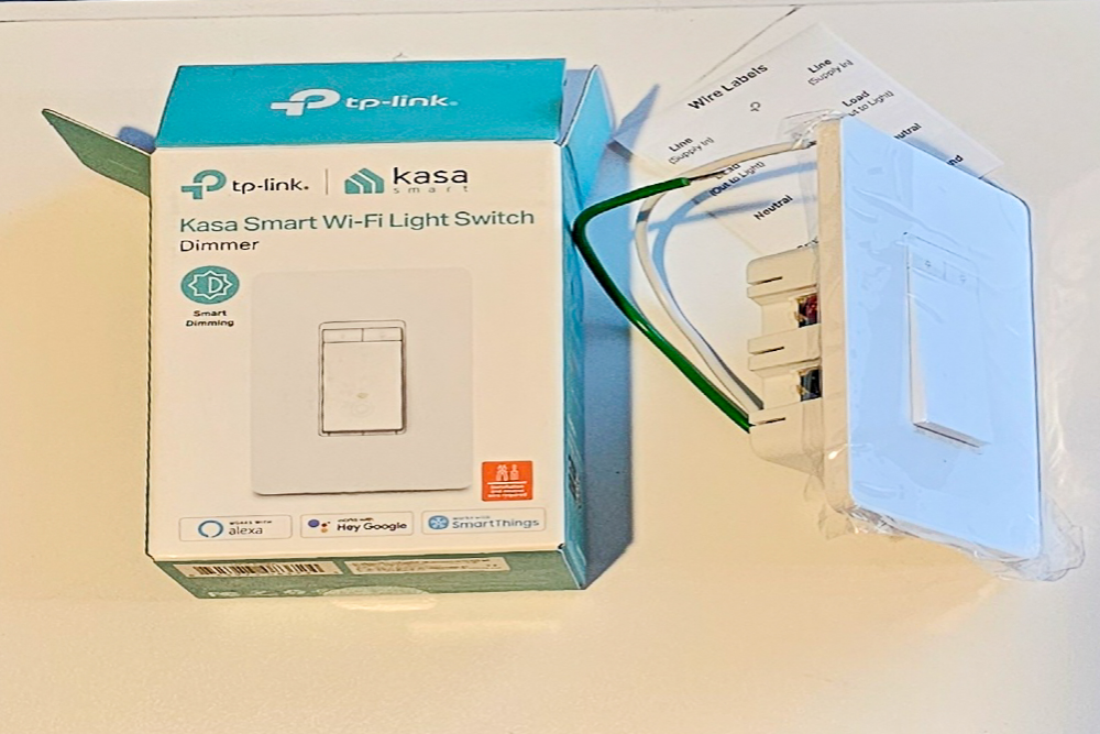 The Kasa Smart Wi-Fi Dimmer Light Switch on a white counter next to its packaging and installation instructions.