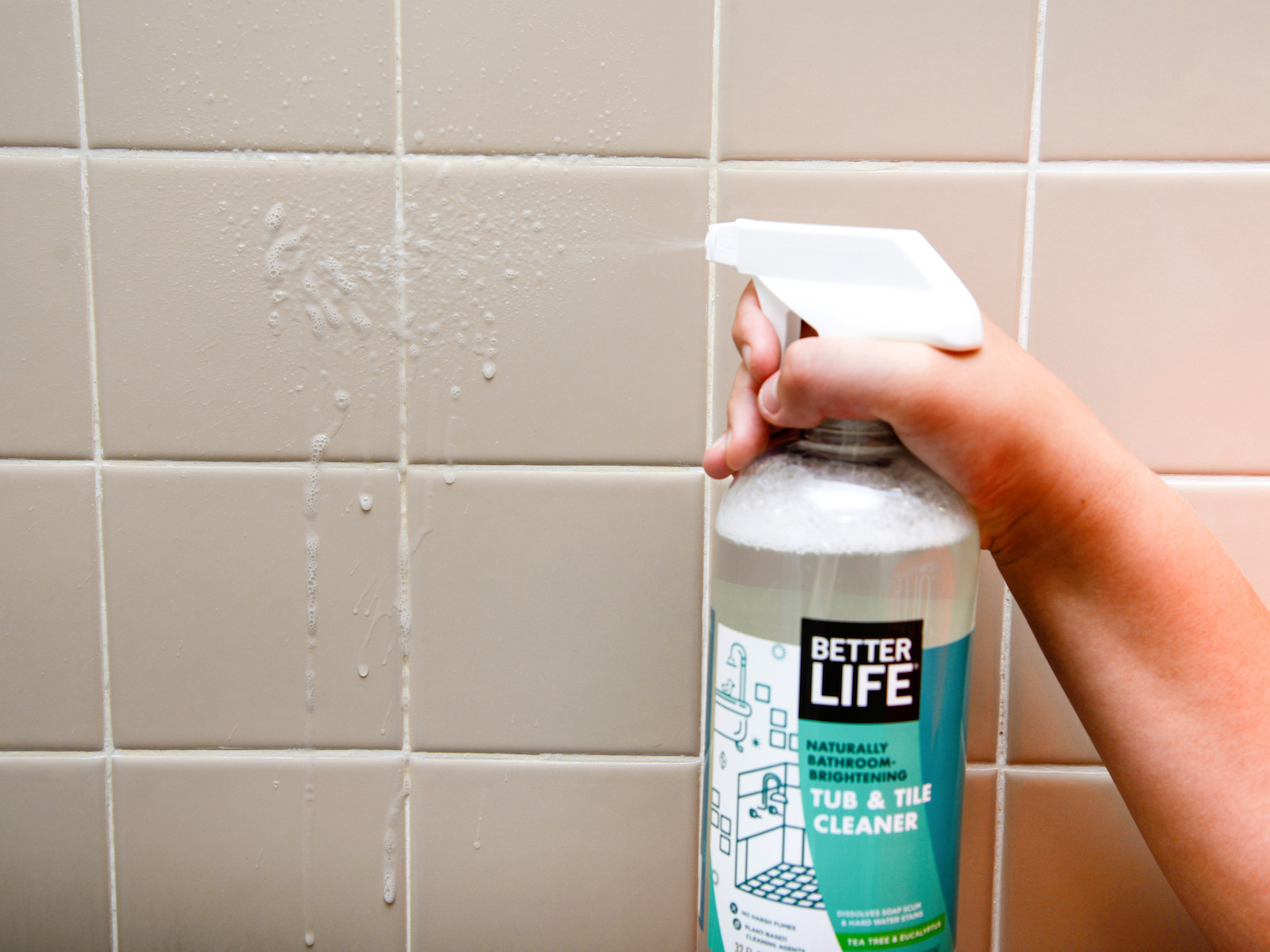 A person spraying the Better Life tub and tile cleaner on shower tile.