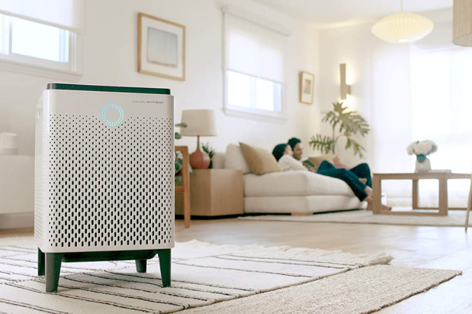 Two people sit comfortably on a couch in the background with the best air purifier for mold option in the foreground cleaning the air