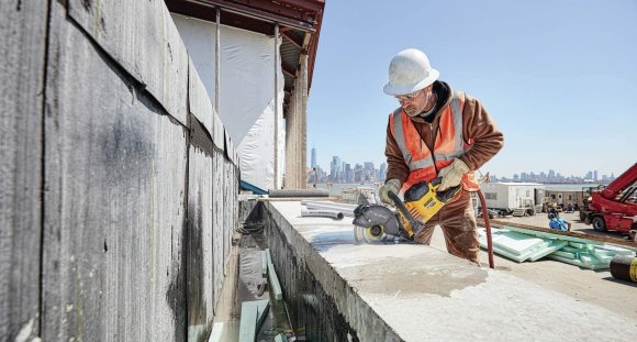 Construction worker sawing through a slab of concrete outside