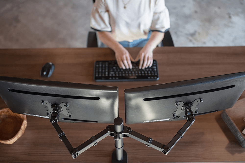 An overhead shot of a person sitting at a desk using the best dual-monitor stand option