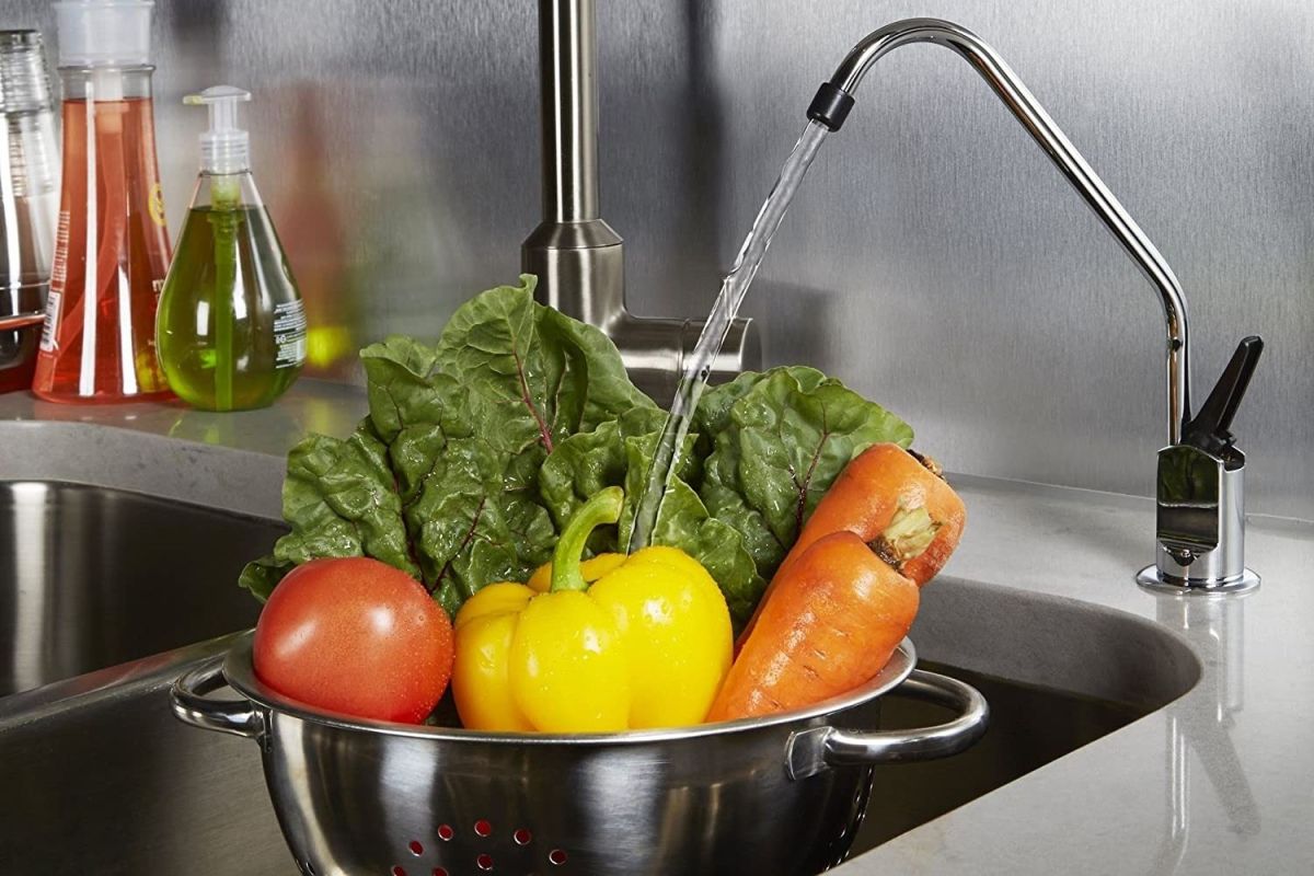 The Best Under Sink Water Filter Option being used to filter water that's spraying down over a colander of raw vegetables
