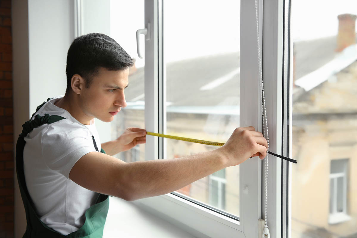 A worker measures the width of a window.