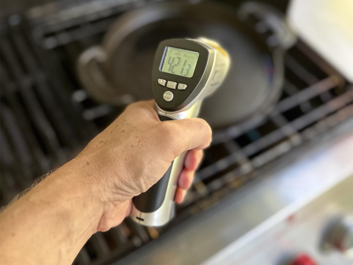 A person testing the surface temperature of a cast iron pan on a grill using the Cuisinart Infrared Surface Thermometer.