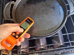 A person testing the surface temperature of a cast iron pan on a grill using the ThermoPro TP420 Meat Thermometer.