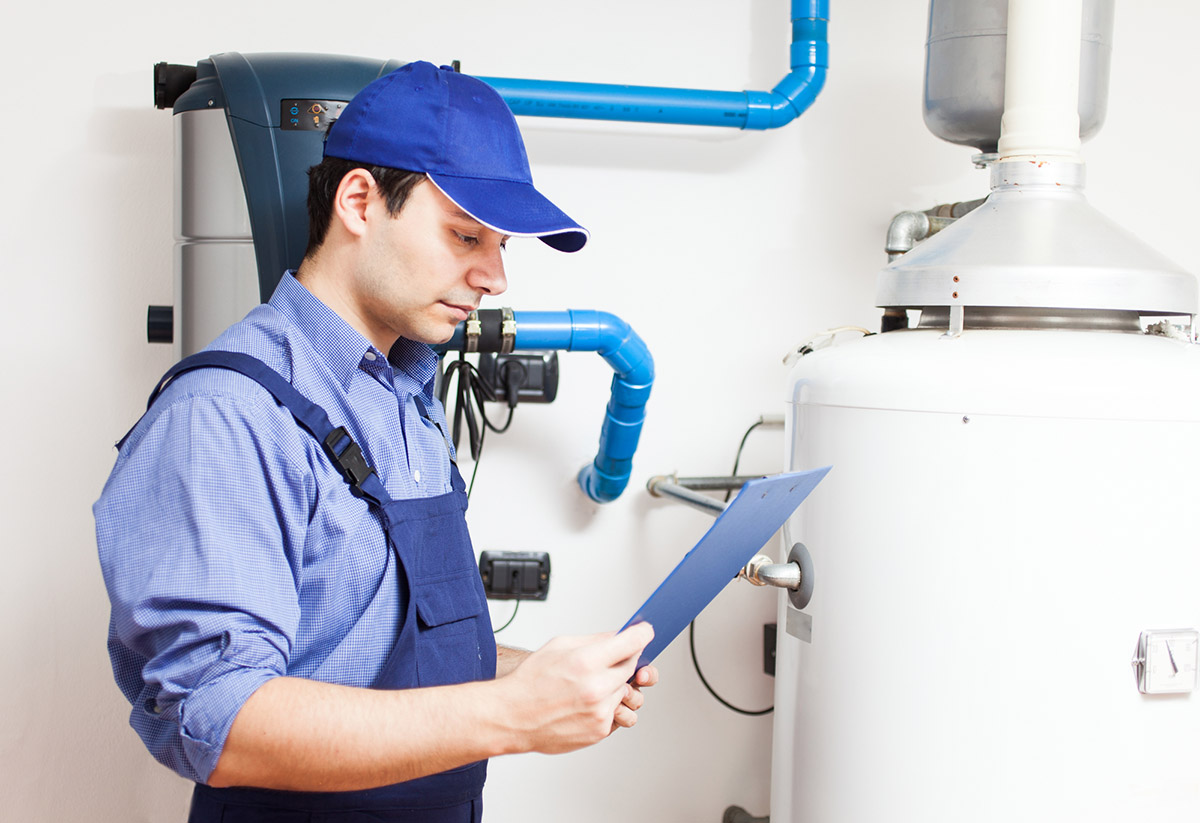 A worker looks at a clipboard while assessing a water heater.