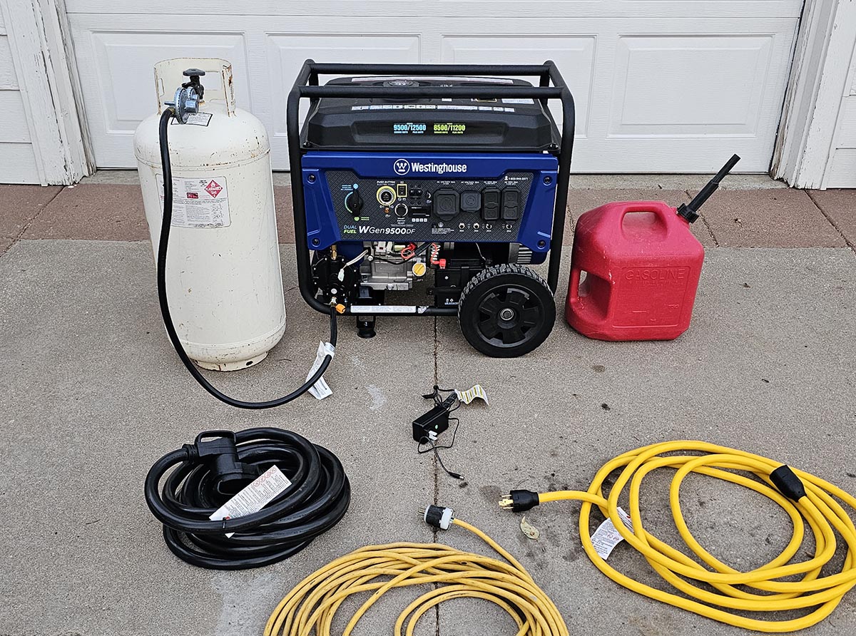 The Westinghouse WGen9500DF Dual-Fuel Generator in a driveway with a gas can, propane tank, and several extension cords next to it.