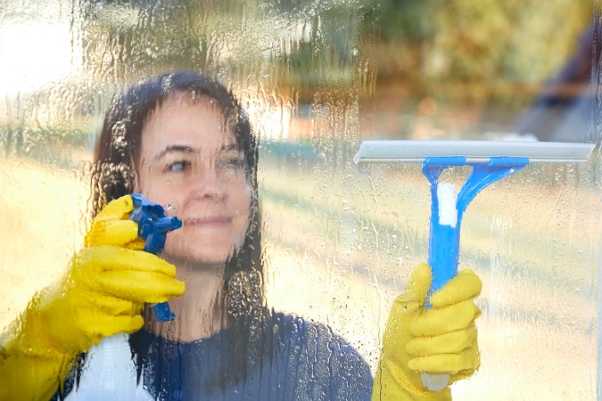 A person cleaning house windows from outside using a homemade window cleaner recipe.
