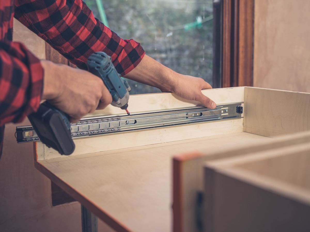 A carpenter uses a small impact driver to drill into a small space on a cabinet.
