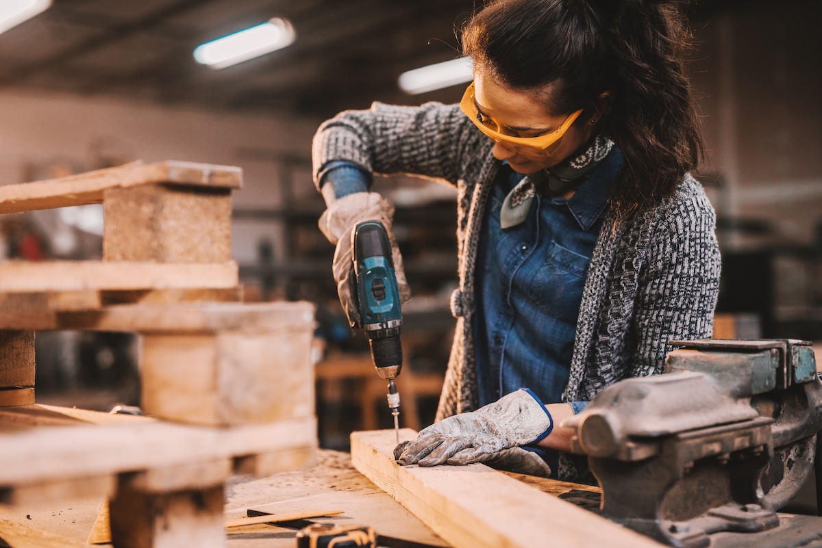 A woman wearing personal safety equipment while using a cordless drill.