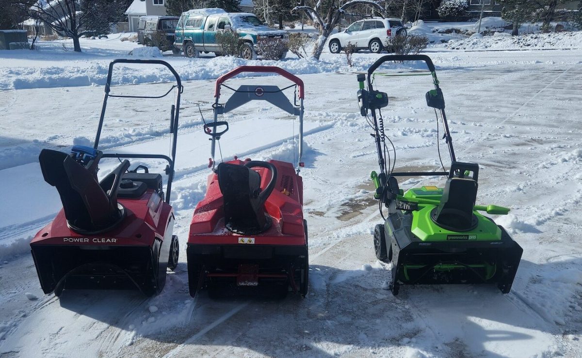 A group of single-stage snow blowers lined up on a snow blown driveway after a storm