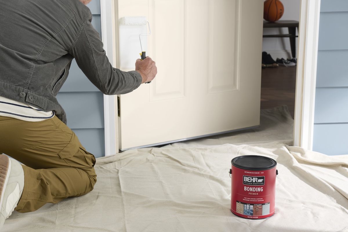 A man in a grey shirt paints a white front door.