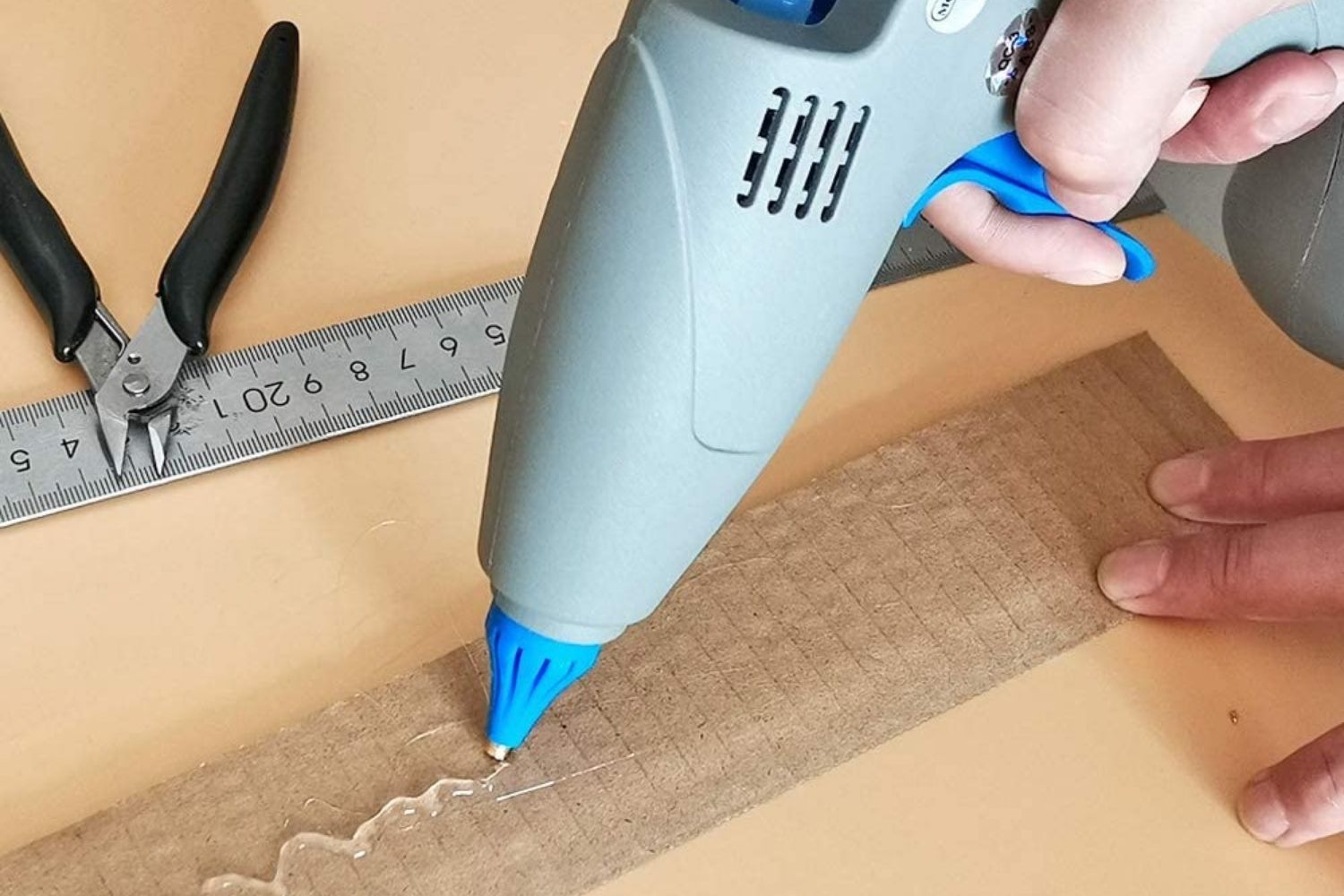 A crafter using the best cordless glue gun option to apply a squiggly line of hot glue on a strip of cardboard