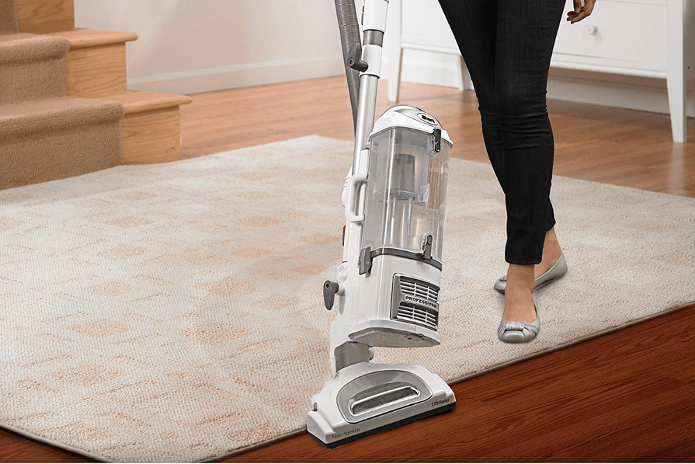A person using the best vacuum for laminate floors to clean the transition between a laminate floor and an area rug.