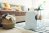 A boho living room scene with a basket of laundry, striped rug, dehumidifier, and couch with pillows.