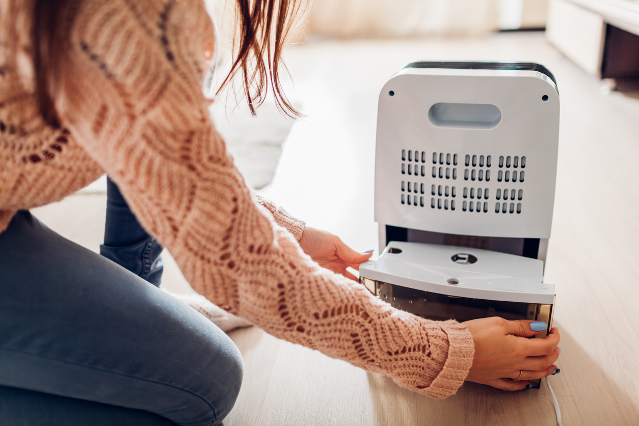 Woman pulls the collection bucket out of the dehumidifier.