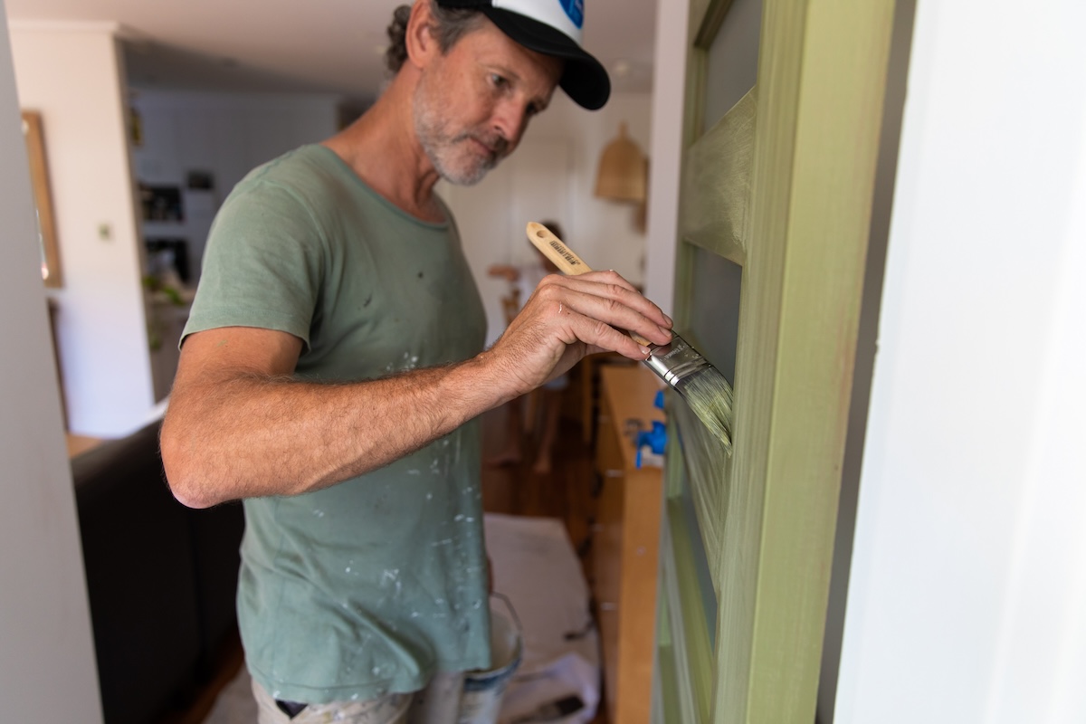 A man paints a front door light sage green.