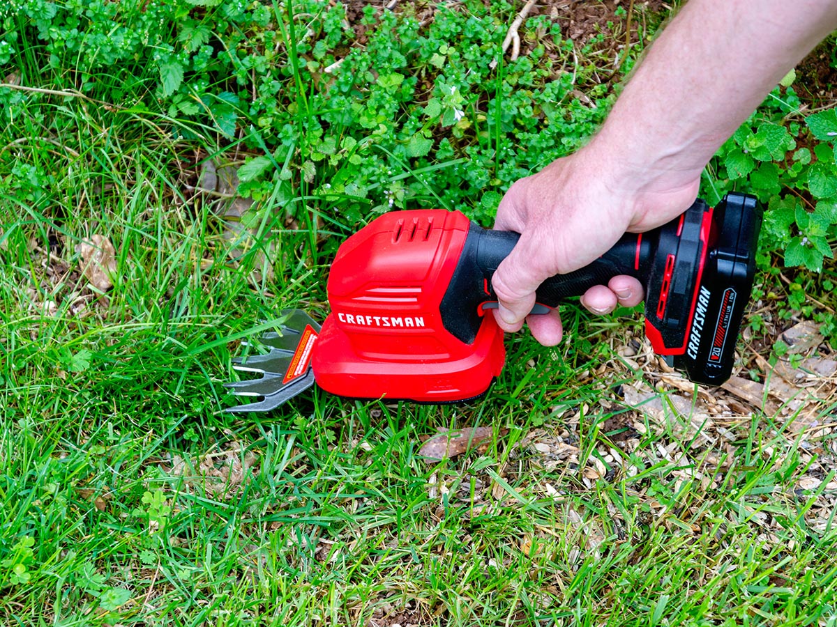 A hand holding the best cordless grass shears option and using it to trim grass