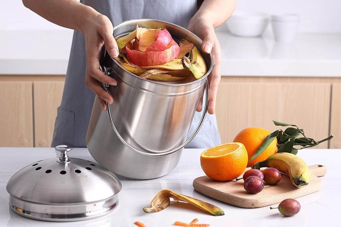 A person tilting the best countertop compost bin option to show it full of fruit peel scraps