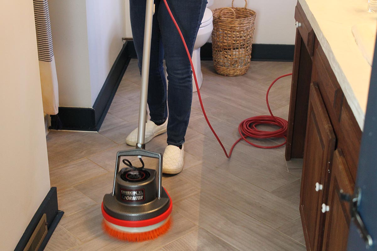 A person using the best floor scrubber option to clean the tile floors in a bathroom.