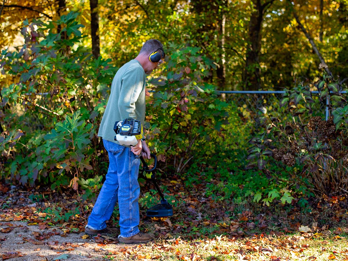 A man using the best gas string trimmer option outside near a large shrub
