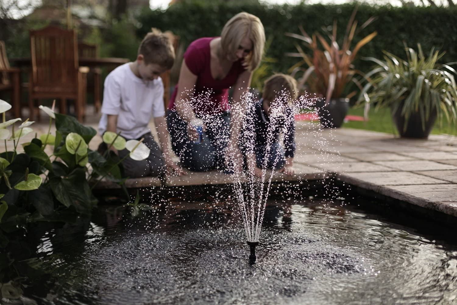 A young family peers into a manmade water feature while the best pond pump creates a small spray in the center of the water