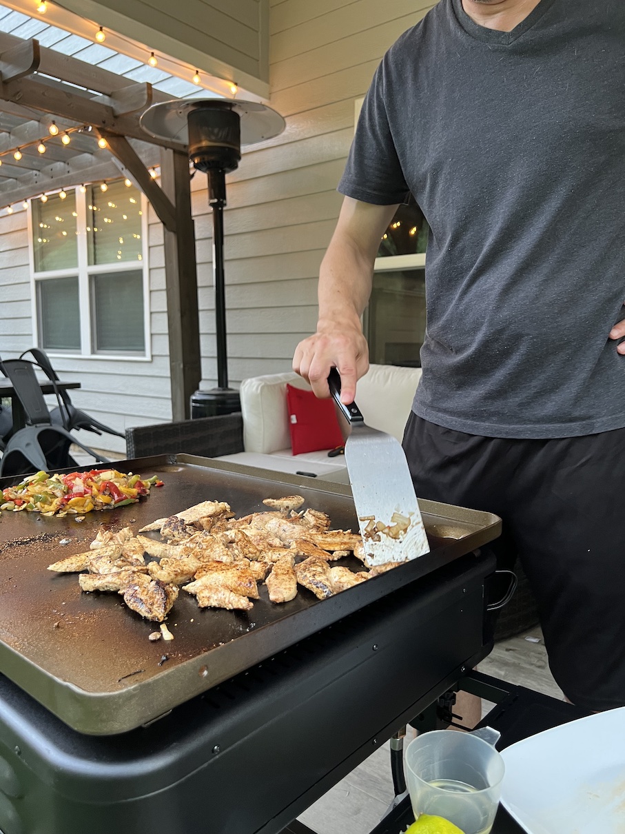 Man cooking chicken and mixed veggies on a flat top grill outdoors
