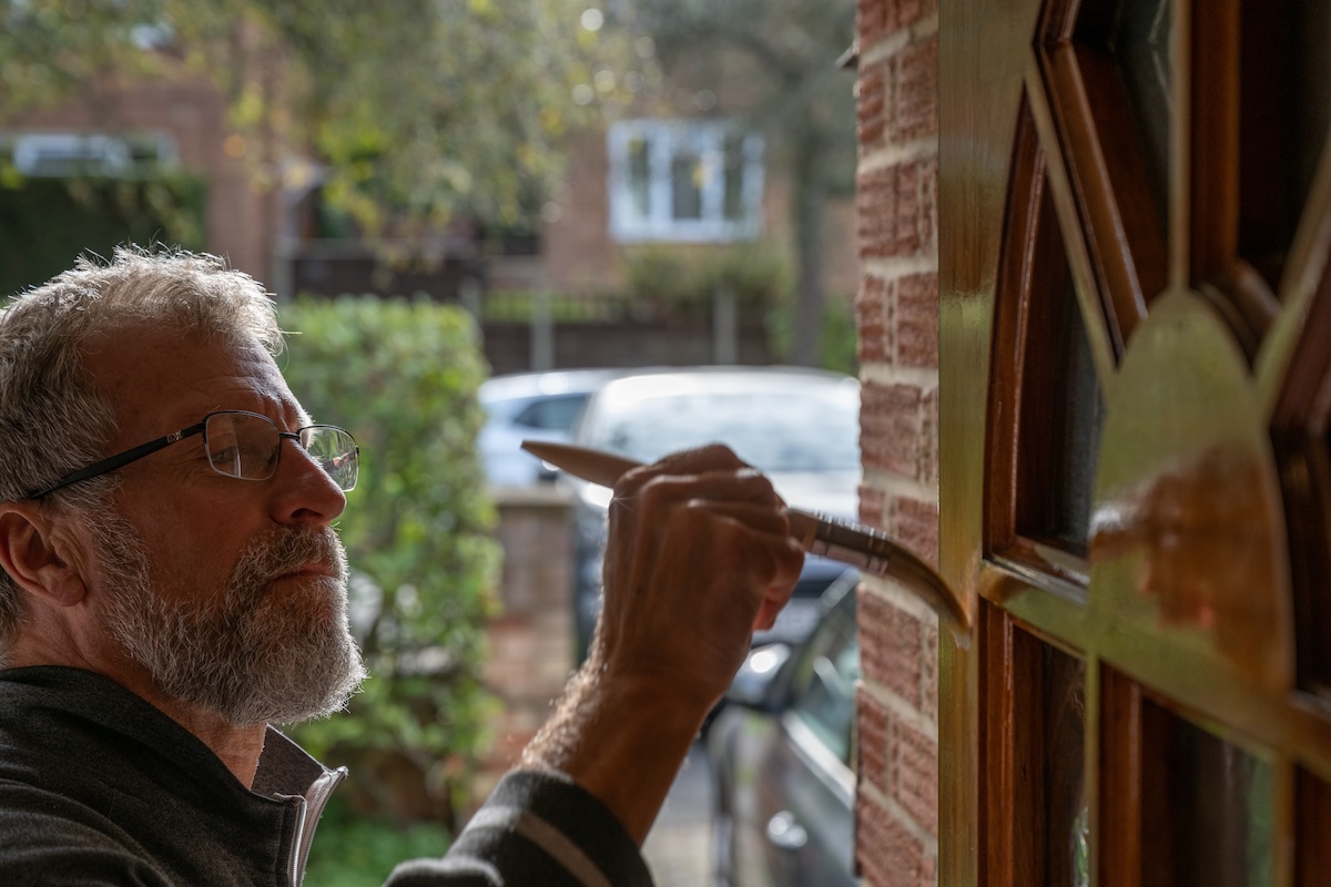 An older gentleman paints a front door with varnish.