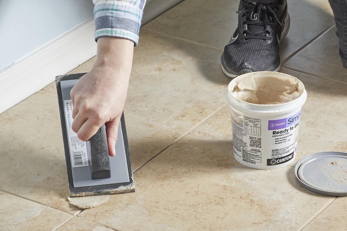 Woman uses grout float to apply new matching grout to existing grout and tile.