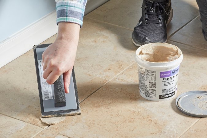 Woman uses grout float to apply new matching grout to existing grout and tile.
