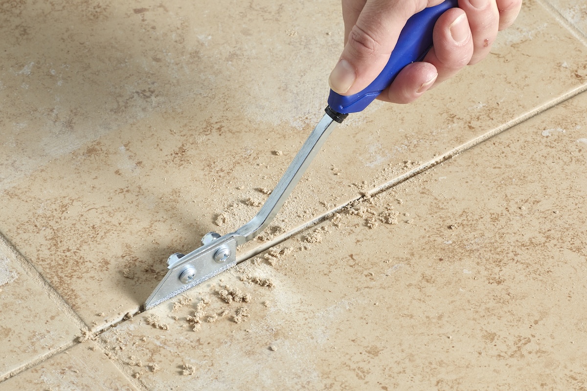 Person uses a grout saw to remove old grout between tile.