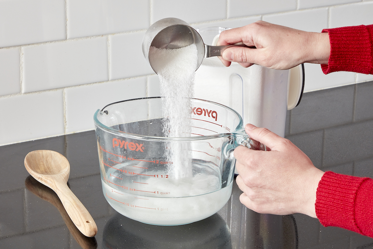 Woman measures white sugar into a measuring cup containing water.
