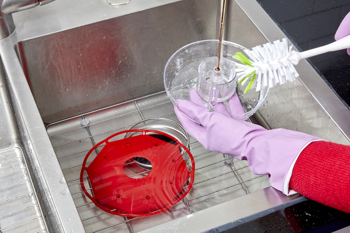 Woman wearing pink rubber gloves cleans hummingbird feeder with cleaning brush.