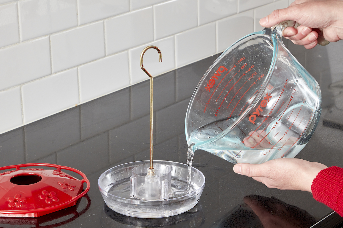 Woman filling a hummingbird feeder with mixture in a glass measuring cup.