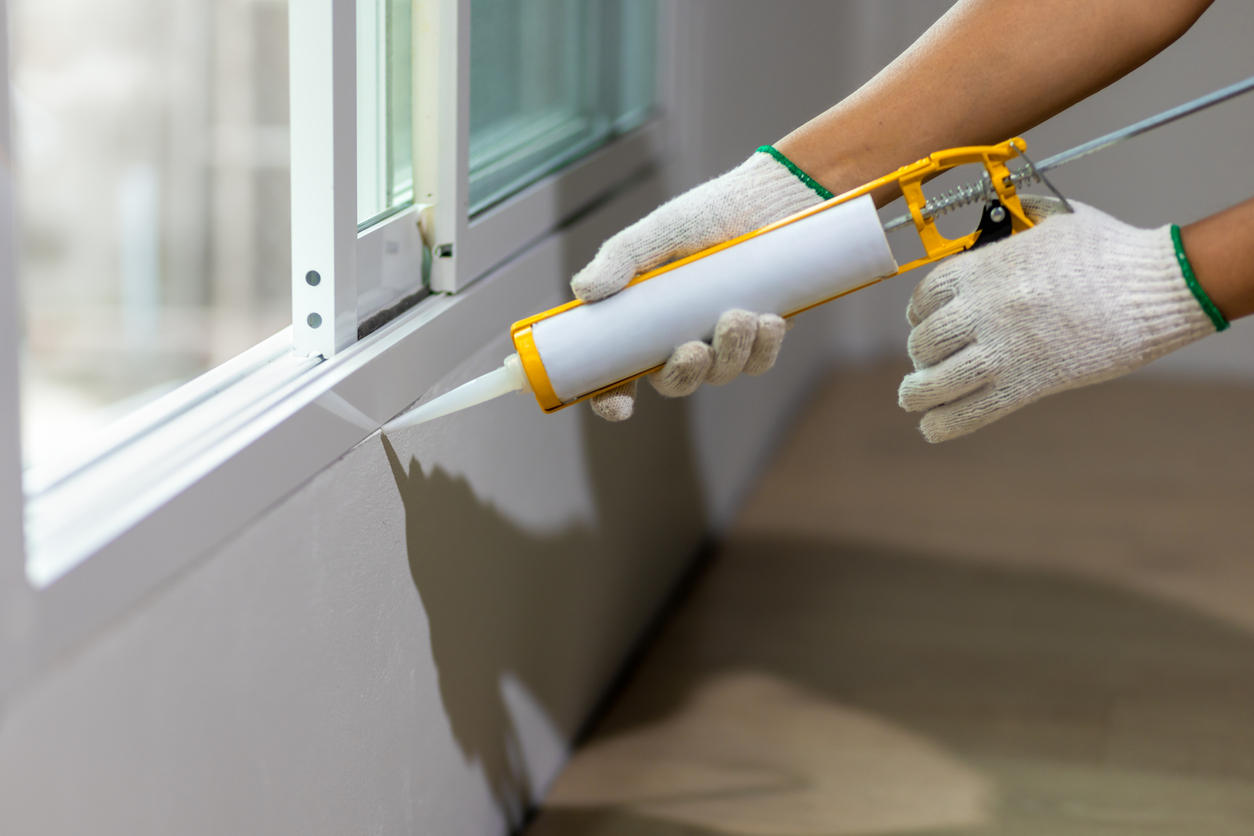 hands in construction gloves sealing a window with caulk sealant