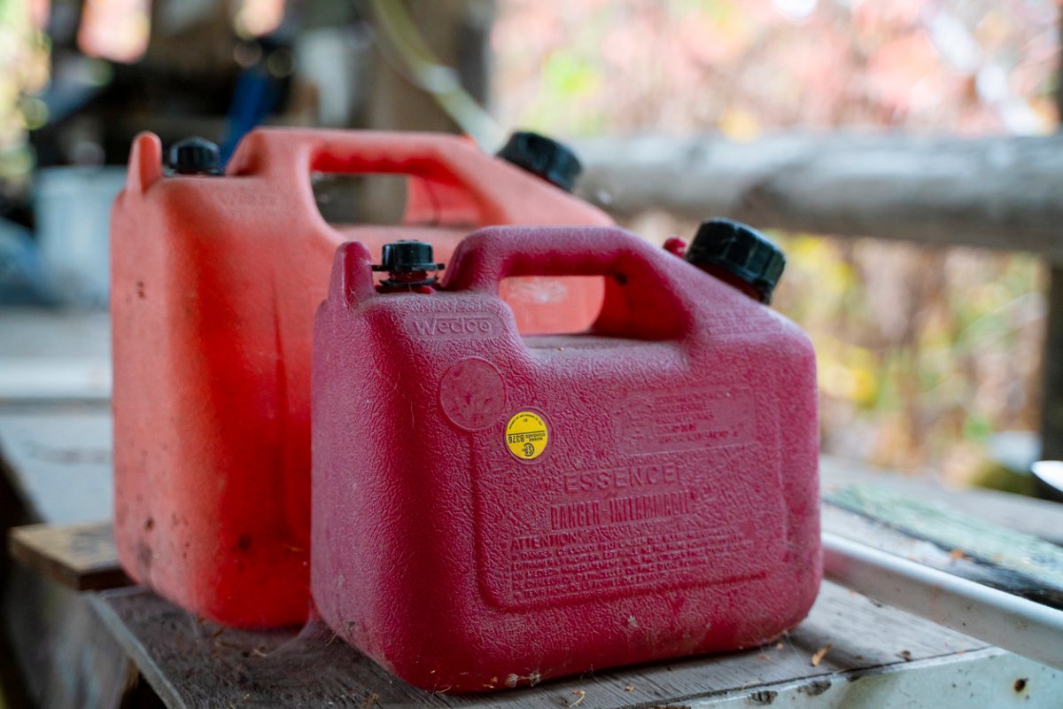 Two red jerry cans for diesel sit next to each other on wooden table outdoors.