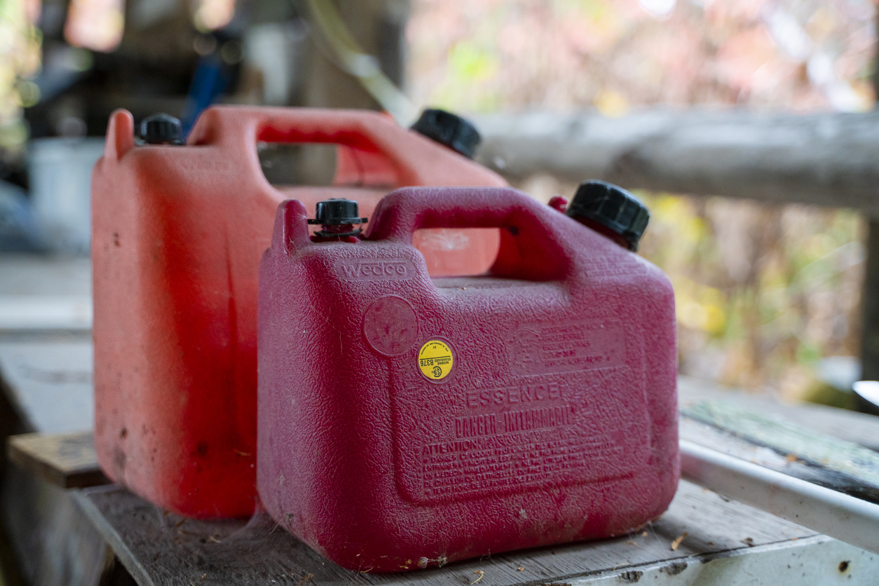 Two red jerry cans for diesel sit next to each other on wooden table outdoors.