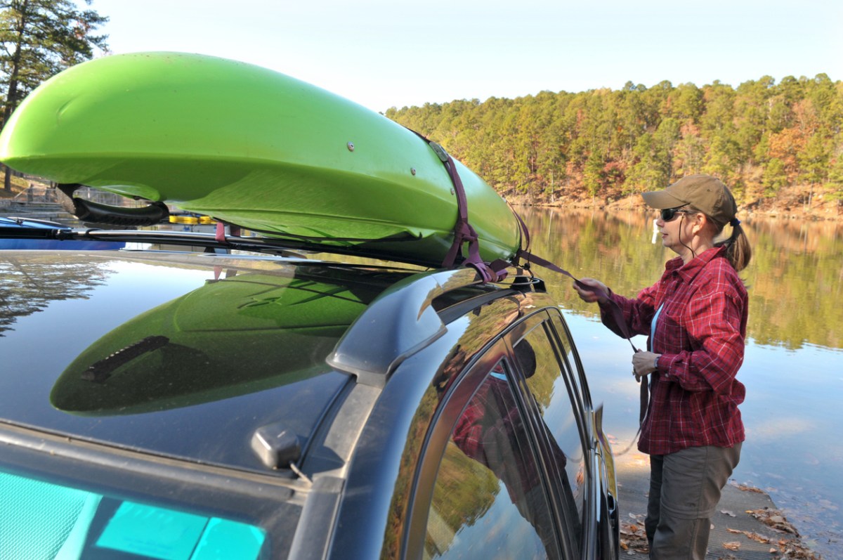 Fit 50-ish woman preparing to unload a kayak from the top of her vehicle.