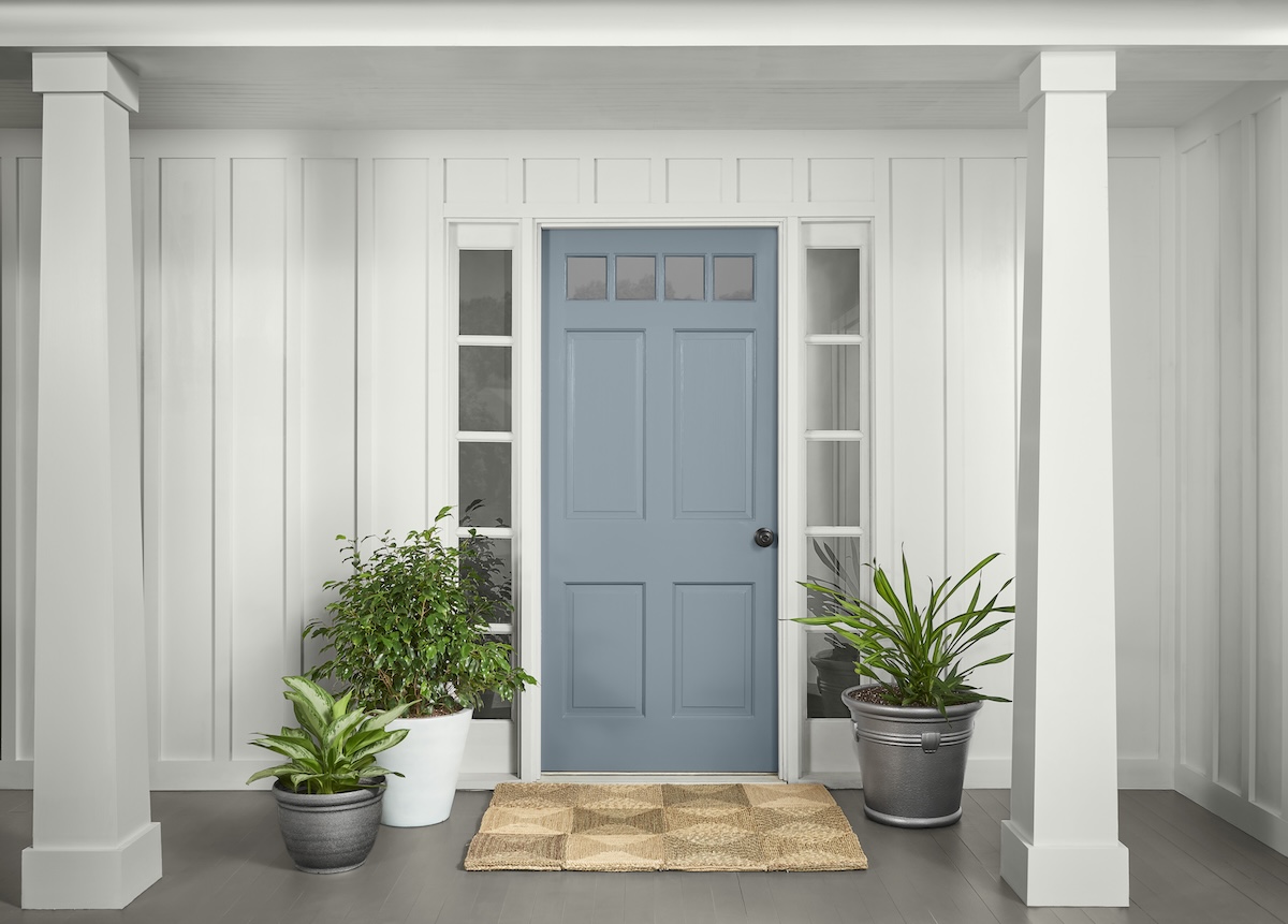 A white house with pillars has a front door painted with BEHR Adirondack Blue paint. The door is surrounded by plants.