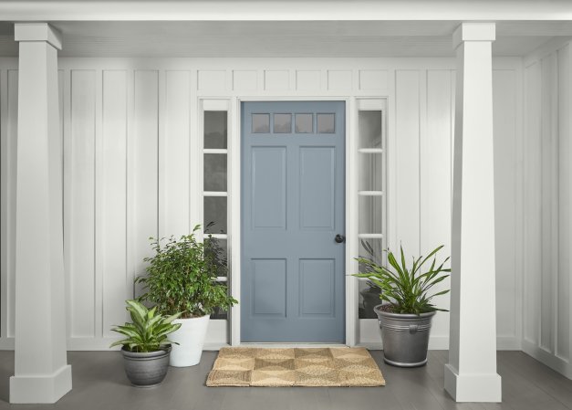A white house with pillars has a front door painted with BEHR Adirondack Blue paint. The door is surrounded by plants.