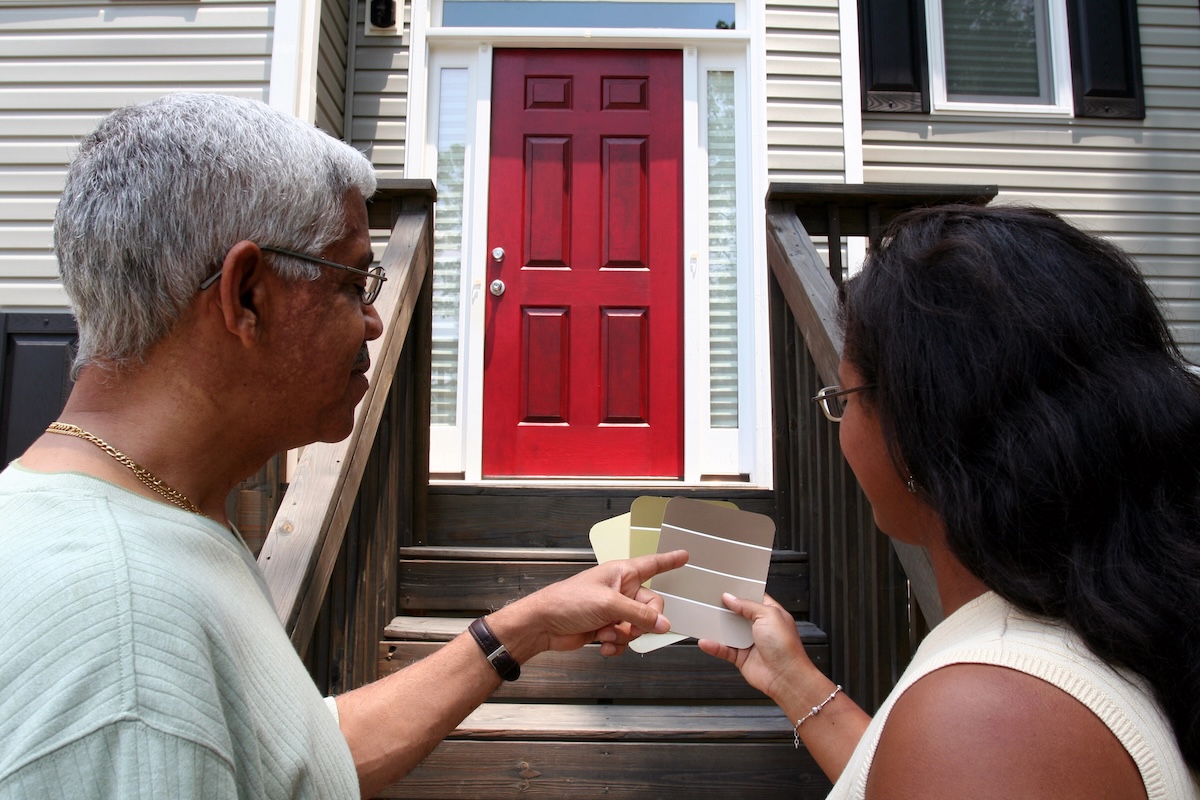 Couple stands outside in front of their front door with paint color chips.