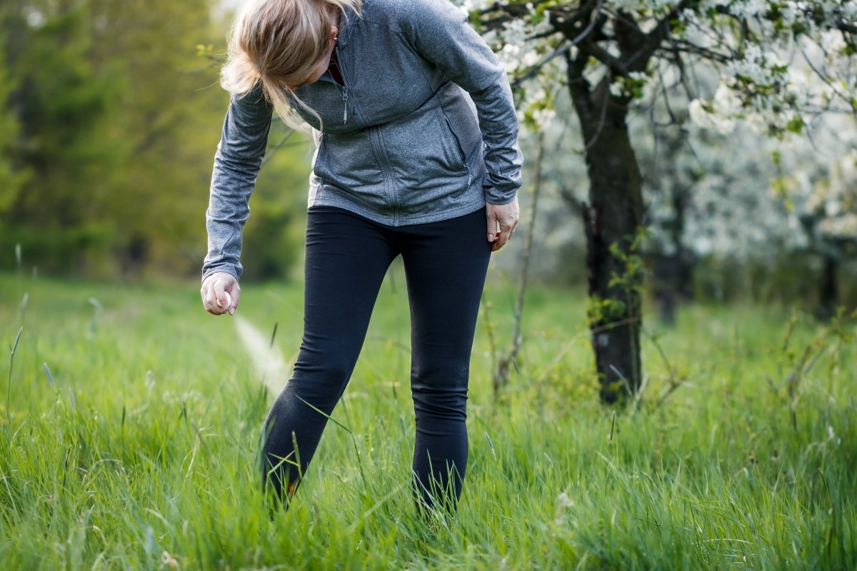 Woman applying insect repellent against ticks on her leg before jogging in spring nature.