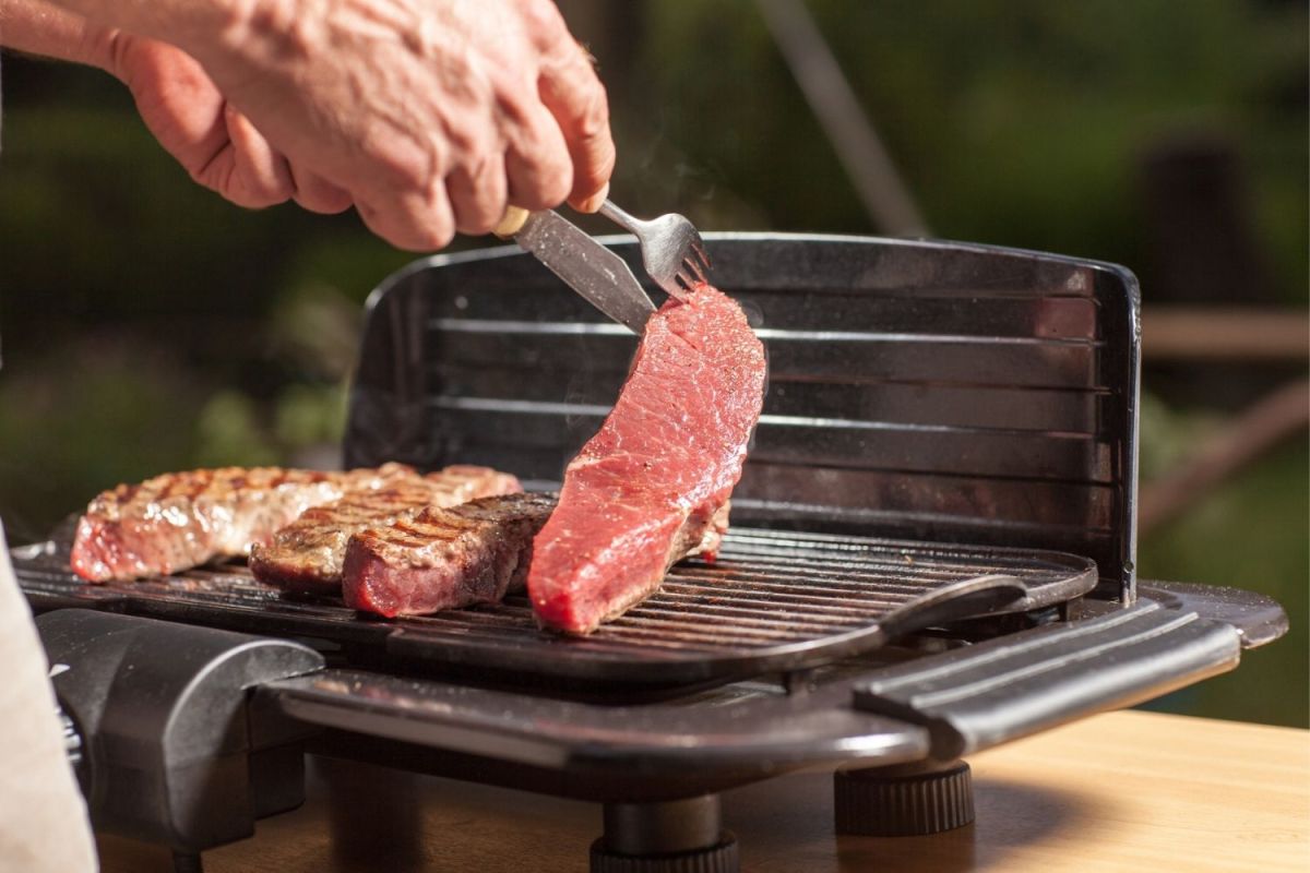 A person using a fork to lift a piece of meat off the best electric grill.