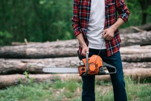 Man from the torso down holding a chainsaw in the outdoors.