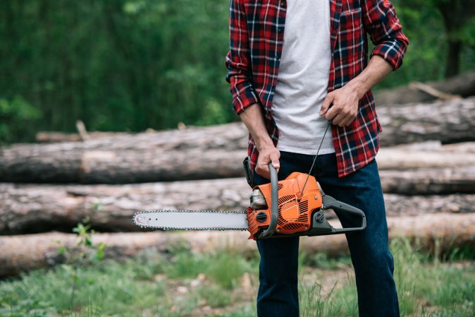 Man from the torso down holding a chainsaw in the outdoors.