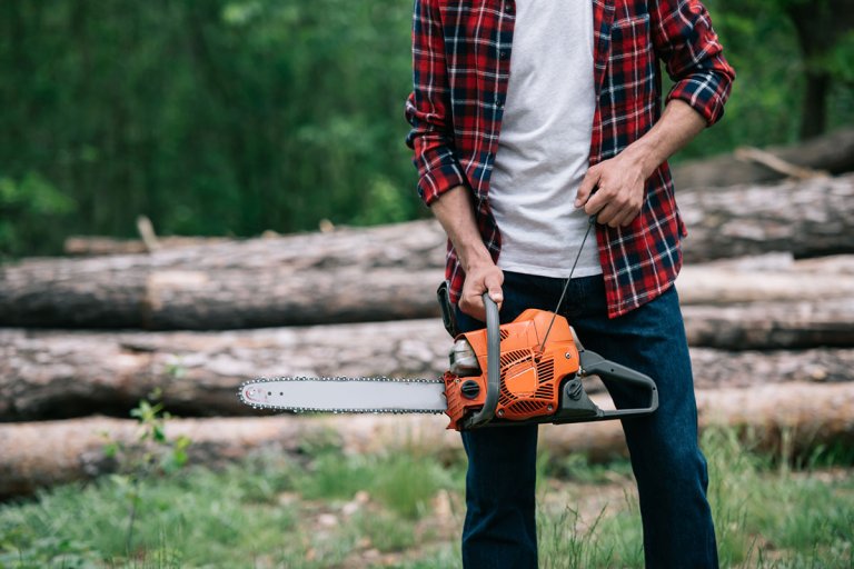 Man from the torso down holding a chainsaw in the outdoors.