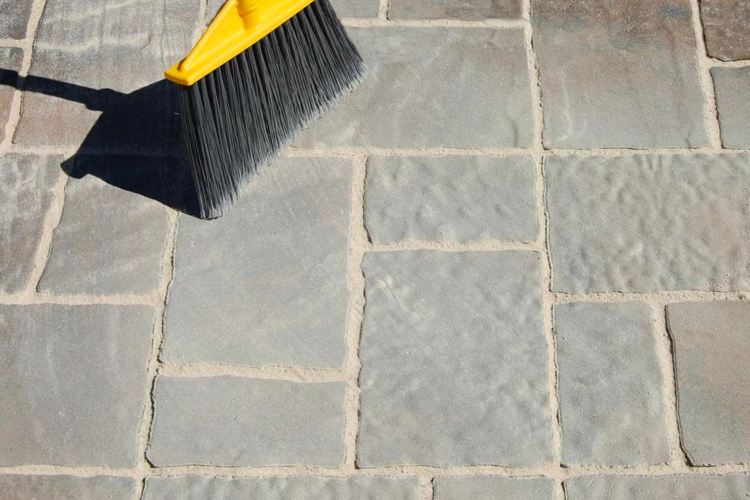 A broom to cleaning excess polymeric sand from between cement patio pavers.