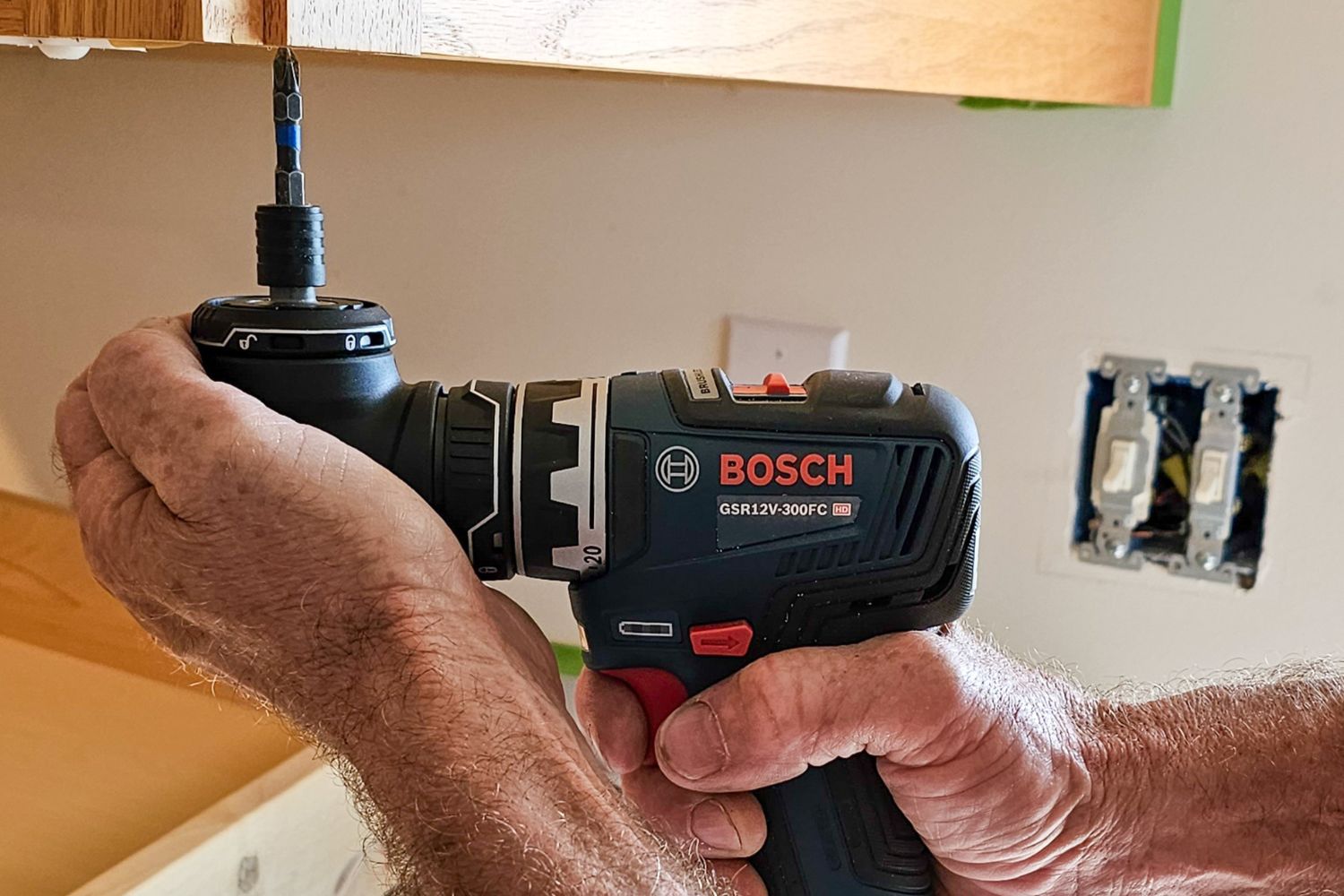 Contractor fastening a screw on the bottom of a cabinet with a Bosch right angle drill.
