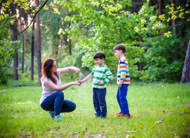 Woman applying spray insect repellent to two young boys' arms